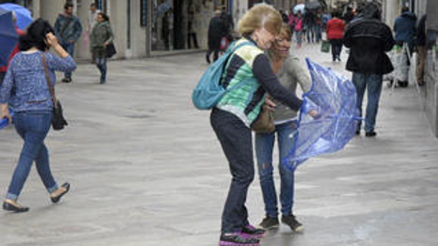 Unas jóvenes tratan de cerrar un paraguas con el viento en Calle Real.