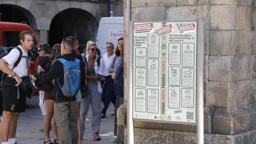 Turistas junto  al cartel de la campaña de buenas prácticas, que Raxoi financió a cargo del plan