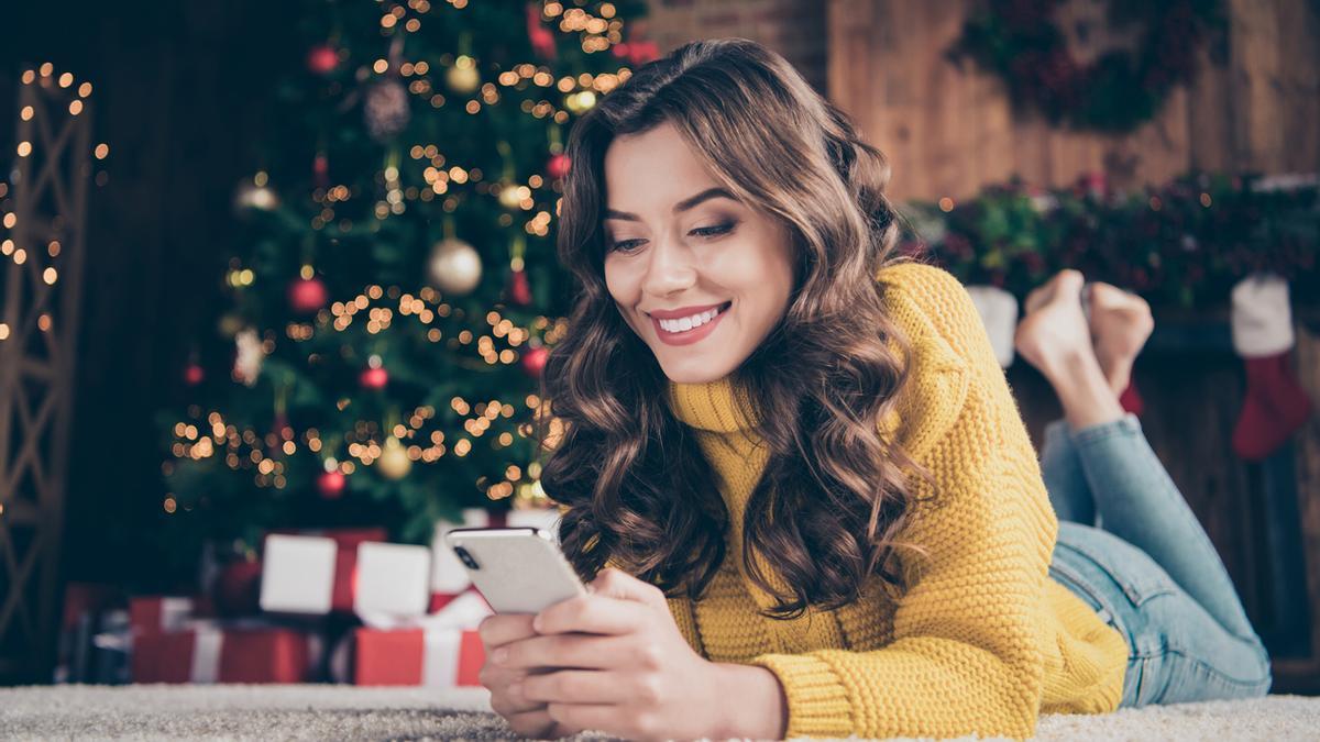 Chica mirando el móvil a los pies del árbol de Navidad