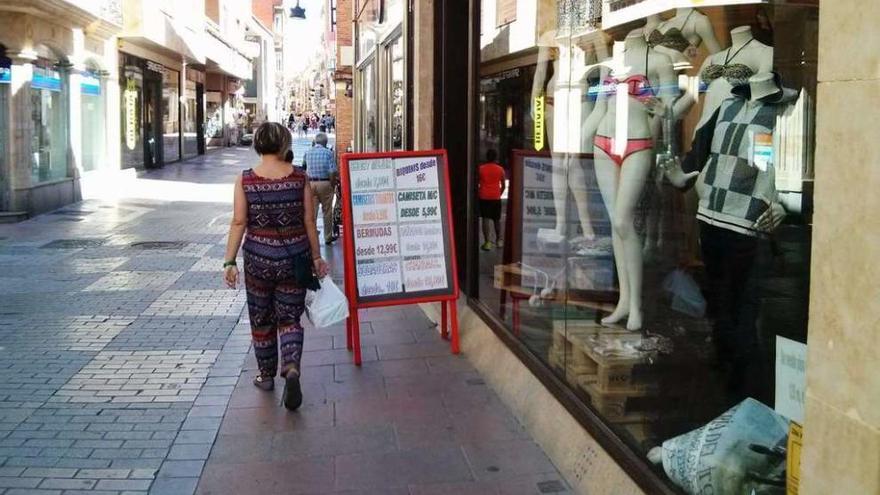 Una mujer se fija en el anuncio de rebajas de una tienda de deportes de la calle Herreros.