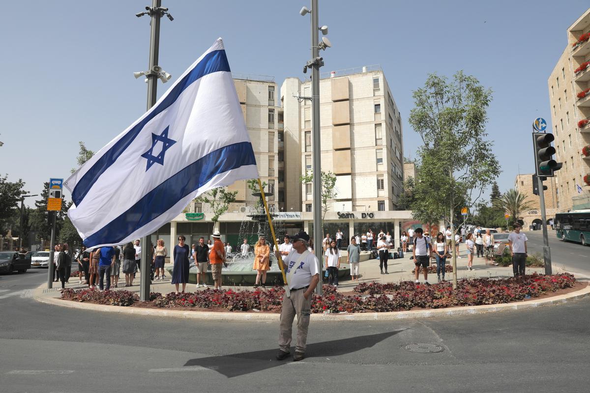 Un hombre ondea una bandera gigante de Israel mientras la gente en la calle se detiene, en el momento en que han sonado sirenas para recordar a las víctimas del holocausto.