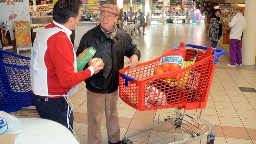 Un hombre entrega alimentos a un voluntario en un hipermercado. // Rafa Vázquez