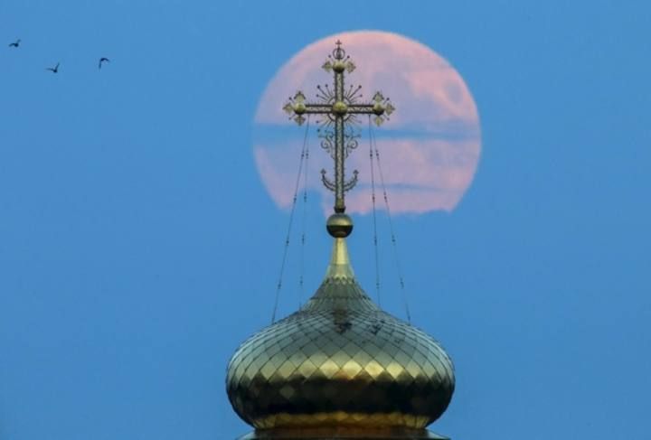 A cross atop of a local monastery stands in front of the moon in the settlement of Poschupovo in Ryazan region