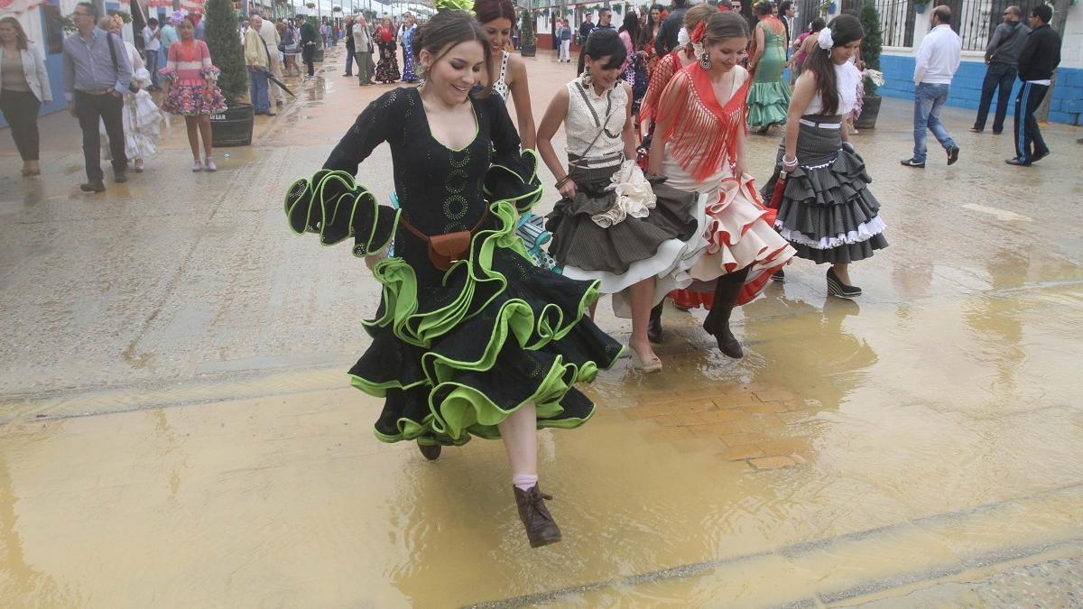 Un grupo de jóvenes cruza un charco en la Feria de Córdoba del 2012, donde también la lluvia hizo acto de presencia.