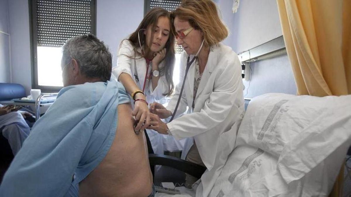 Una residente atiende a un paciente en la habitación del hospital.