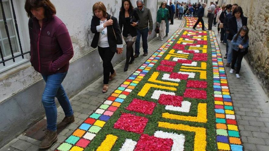 Varios voluntarios ultiman los detalles de una alfombra ante la mirada de los visitantes.