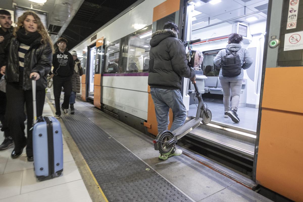 Un viajero sube un patinete eléctrico a bordo de un tren en la estación de Catalunya