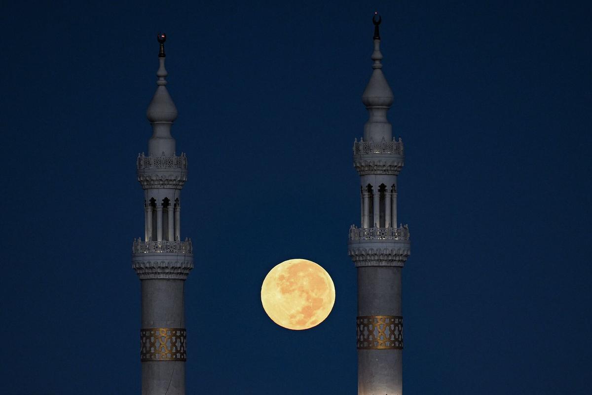 TOPSHOT - The full moon sets behind a mosque in El-Shorouk, a satellite city on the eastern outskirts of Cairo, early on October 7, 2025. (Photo by Khaled DESOUKI / AFP)
