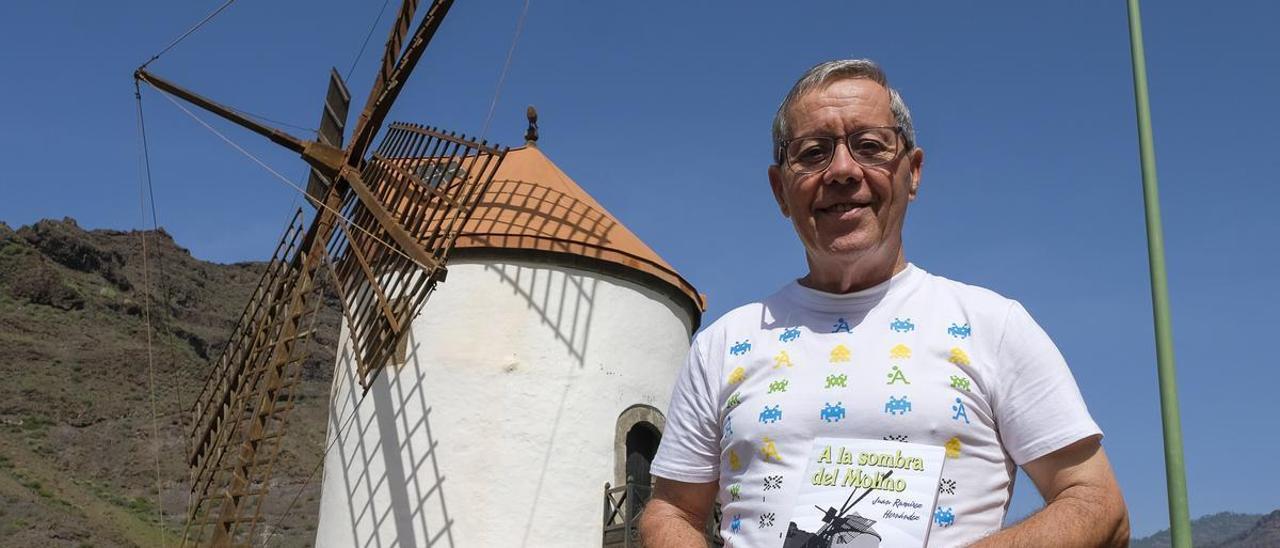 Juan Ramírez sostiene un ejemplar de su libro frente al Molino de Viento de Mogán.