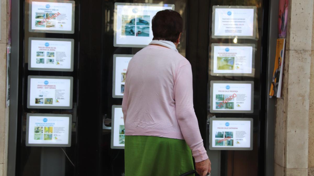 Una dona revisa les ofertes de pisos a la venda fora d'una immobiliària.