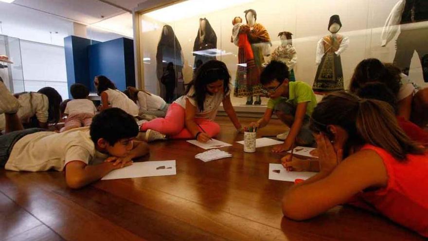 Los niños dibujan frente a unos trajes tradicionales.