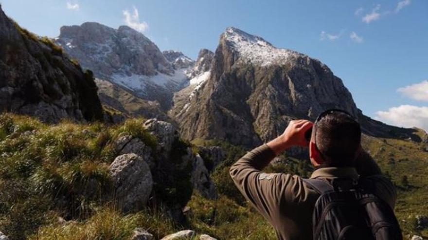 Un agente de Medio Ambiente de Baleares mira con unos prismáticos hacia las montañas nevadas de la Serra.