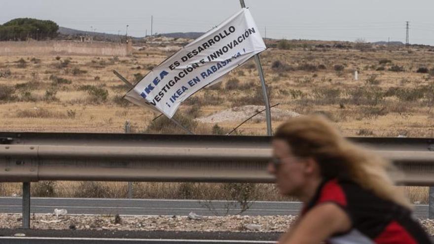 Una ciclista pasa por delante de los terrenos de Rabasa, donde se ve un cartel sobre Ikea