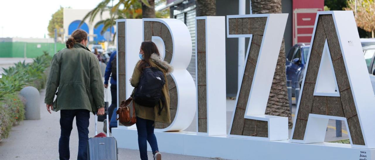 Dos viajeros pasan frente al cartel ‘Ibiza’ de reclamo situado frente a la fachada del aeropuerto de Eivissa. | VICENT MARÍ