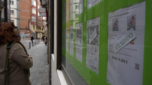Una mujer mira anuncios de venta de pisos en la fachada de una inmobiliaria en Zamora.