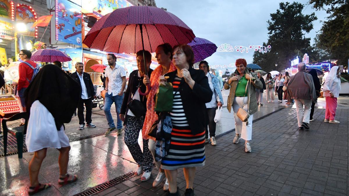 Gente con paraguas entre las atracciones festivas
