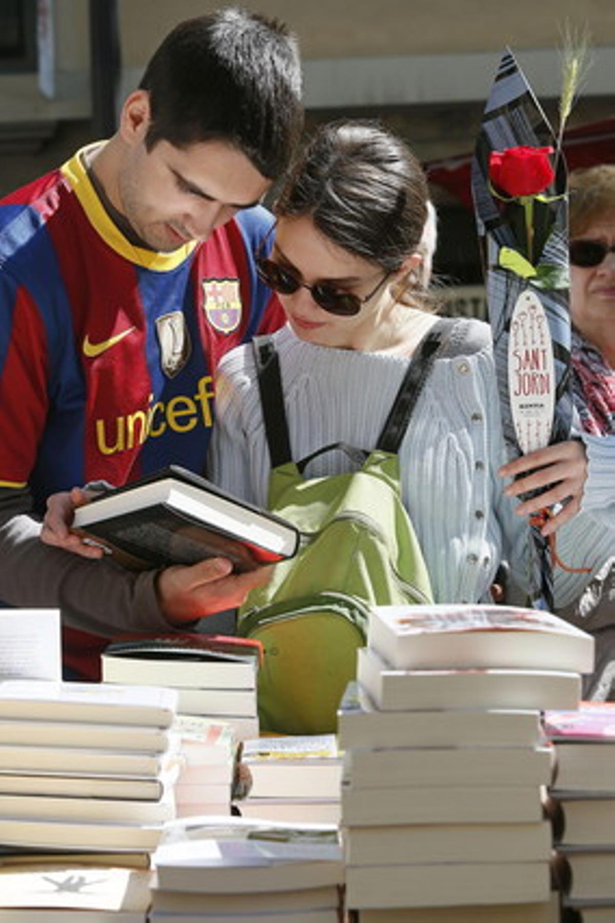 Una pareja, ella con una rosa y él con una camiseta del Barça, en una parada de libros en las Ramblas de Barcelona durante la Diada de Sant Jordi.