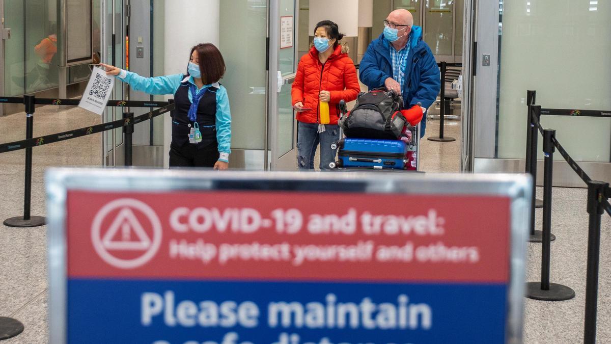 Pasajeros pasan frente a una señal de advertencia del Covid en el aeropuerto de Toronto