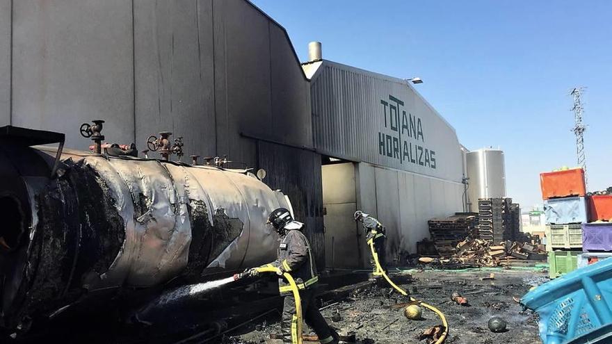 Dos bomberos en el momento de apagar el fuego de la nave industrial de Totana.