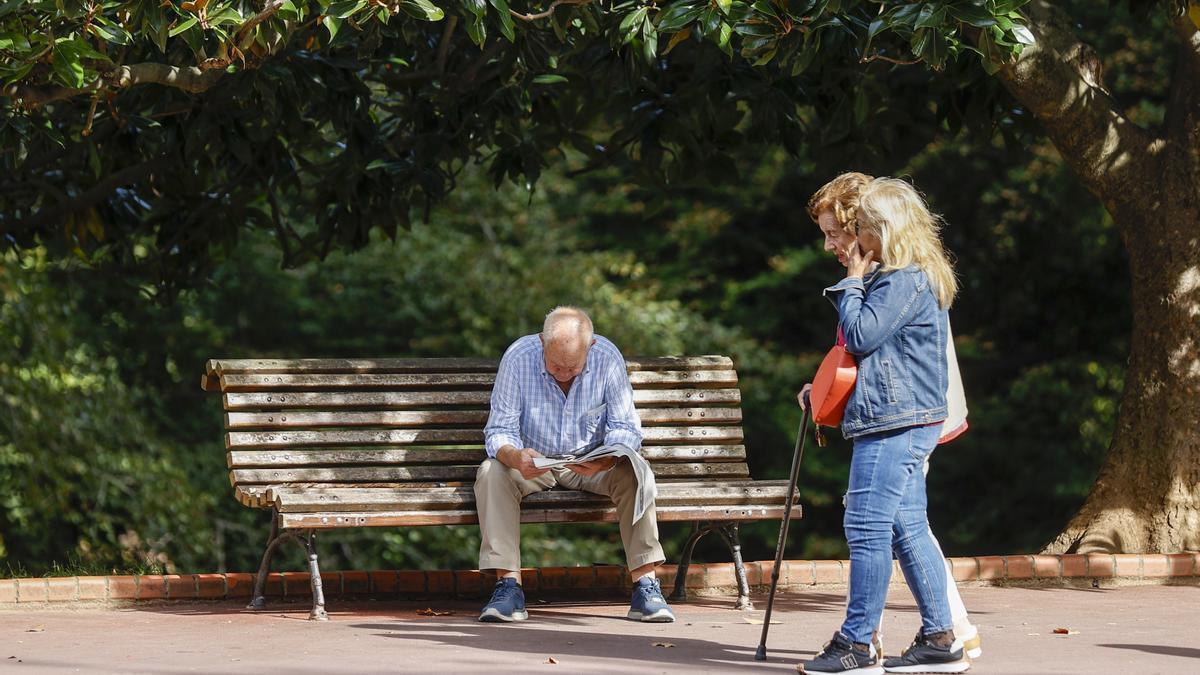 Un pensionista lee el periódico en un banco de un parque.
