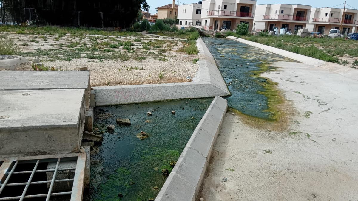 La arqueta, el agua verde que fluye y, al fondo, la calle 8 de Marzo de Sant Joan