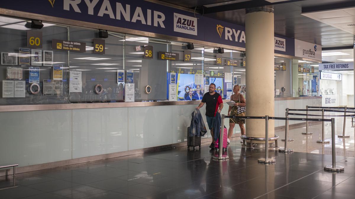 Archivo - Dos personas pasan junto a una ventanilla de Ryanair en el Aeropuerto del Prat.
