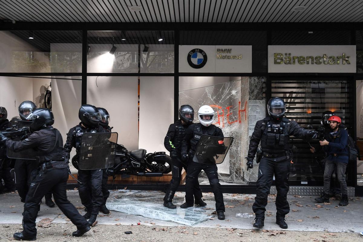 Los miembros de la Brigada Motorizada para la Represión de la Acción Violenta (BRAV) esperan cerca de una tienda BMW dañada mientras se producen enfrentamientos con los manifestantes durante una manifestación en París, el 18 de octubre de 2022