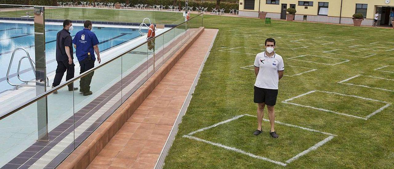 Trabajadores del Centro Asturiano finalizan la adecuación de las piscinas exteriores. El socorrista David Maseda posa de pie en una de las cuadrículas de la zona verde que se marcaron ayer para que los usuarios puedan mantener la distancia de seguridad.