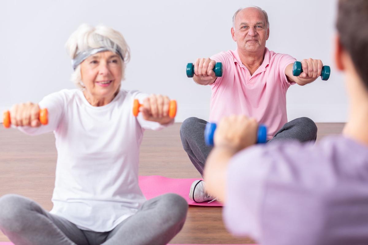 FOTO BAJADA DE 123RF EL 19 DE SEPTIEMBRE DEL 2022. DOS ABUELOS, GENTE MAYOR, HACIENDO DEPORTE, EJERCICIO. TERCERA EDAD, DEPORTE, ESTAR EN FORMA. Couple of active seniors during exercises on gym with young instructor. FOTO DE 123RF