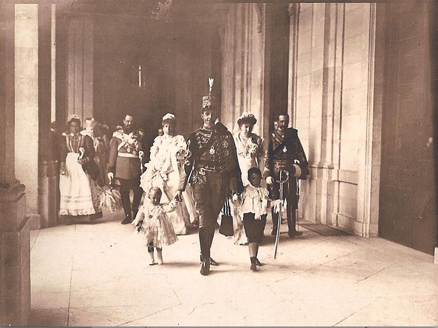 Foto de hacia 1911 de un joven Alfonso XIII con dos de sus hijos, posiblemente los infantes Alfonso y Jaime, por el Palacio Real. Detrás la Reina Victoria Eugenia y la Reina Madre María Cristina.