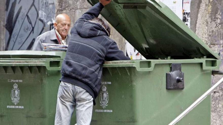 Un hombre rebusca en un contenedor de basura.