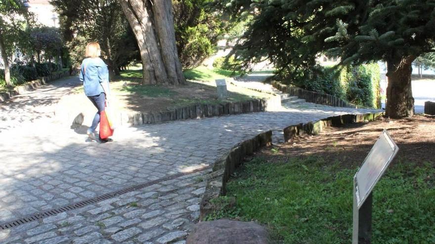 Una mujer camina por el jardín botánico, donde se aprecian varios identificadores de árboles que han sido borrados por el paso del tiempo.