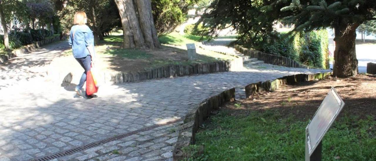 Una mujer camina por el jardín botánico, donde se aprecian varios identificadores de árboles que han sido borrados por el paso del tiempo.