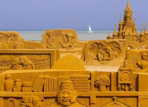 A sailing boat is seen behind sand sculptures during the Sand Sculpture Festival Frozen Summer Fun in Ostend