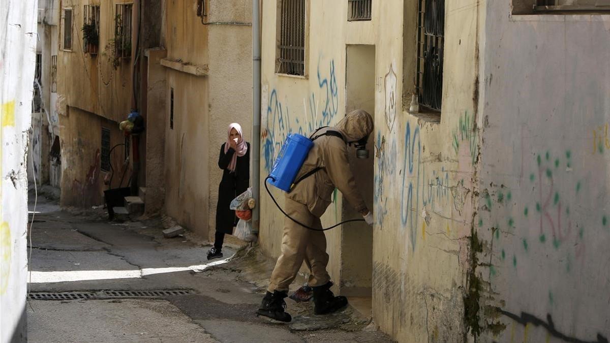 Una mujer palestina cubre su cara con un pañuelo mientras un trabajador de protección civil desinfecta un portal, el pasado día 16 de marzo.