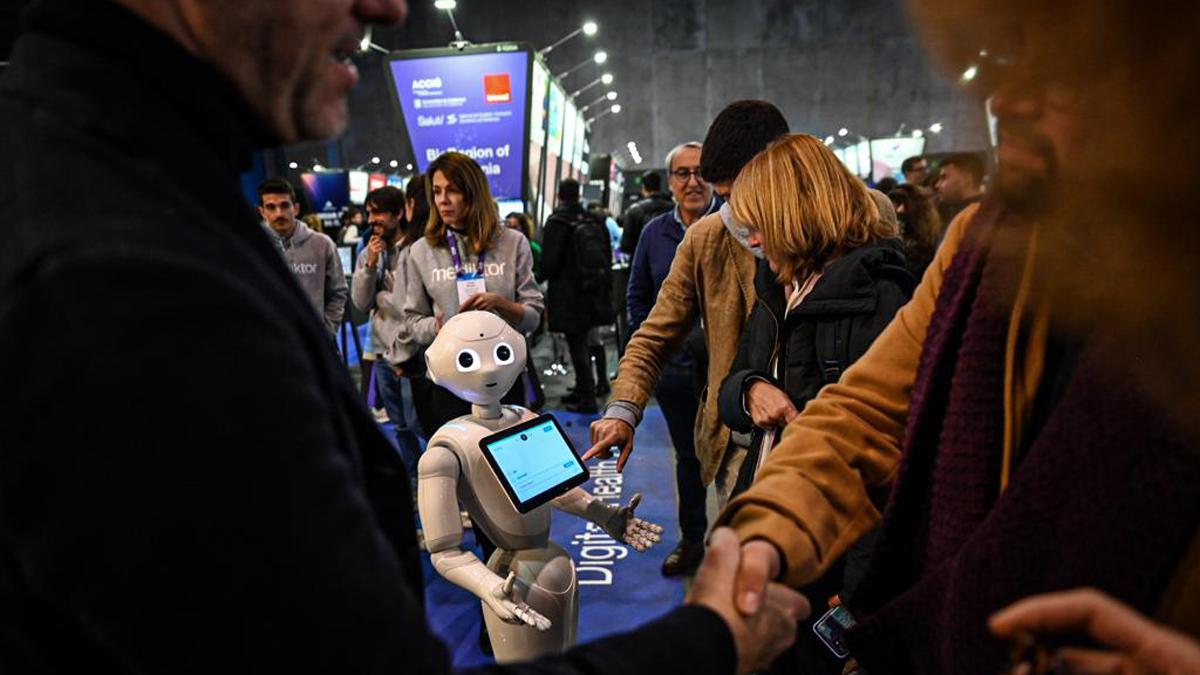 Dos asistentes al MWC 2023 se saludan, ante la atenta mirada de un robot