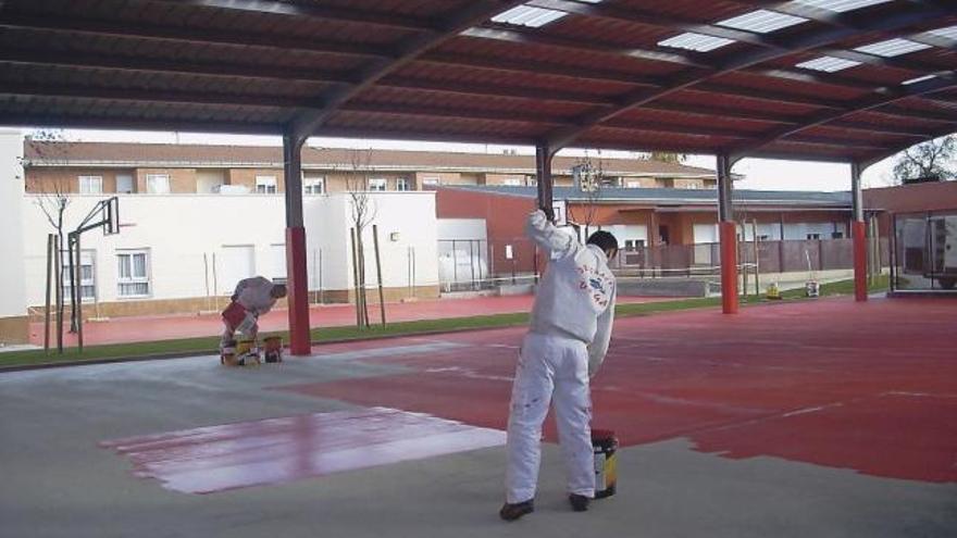 Los operarios pintando el suelo de la pista deportiva del colegio de Morales del Vino.