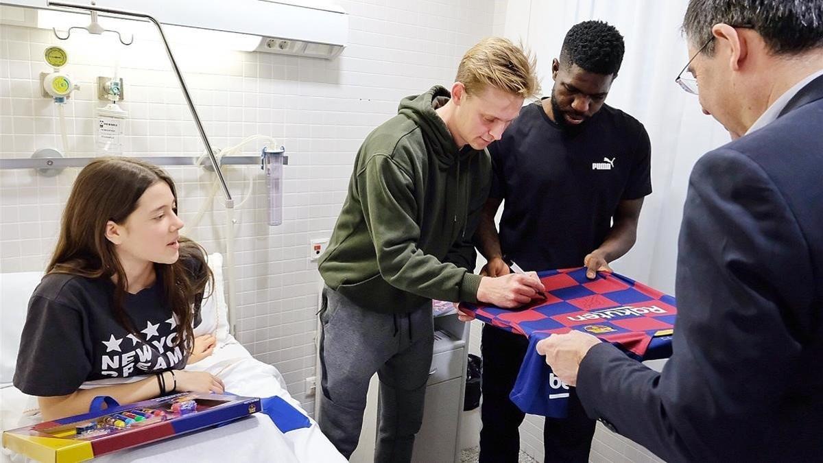 Frenkie de Jong firma una camiseta que sostienen Samuel Umtiti y Josep Maria Bartomeu, el presidente del Barça, en el Hostpital de Nens.