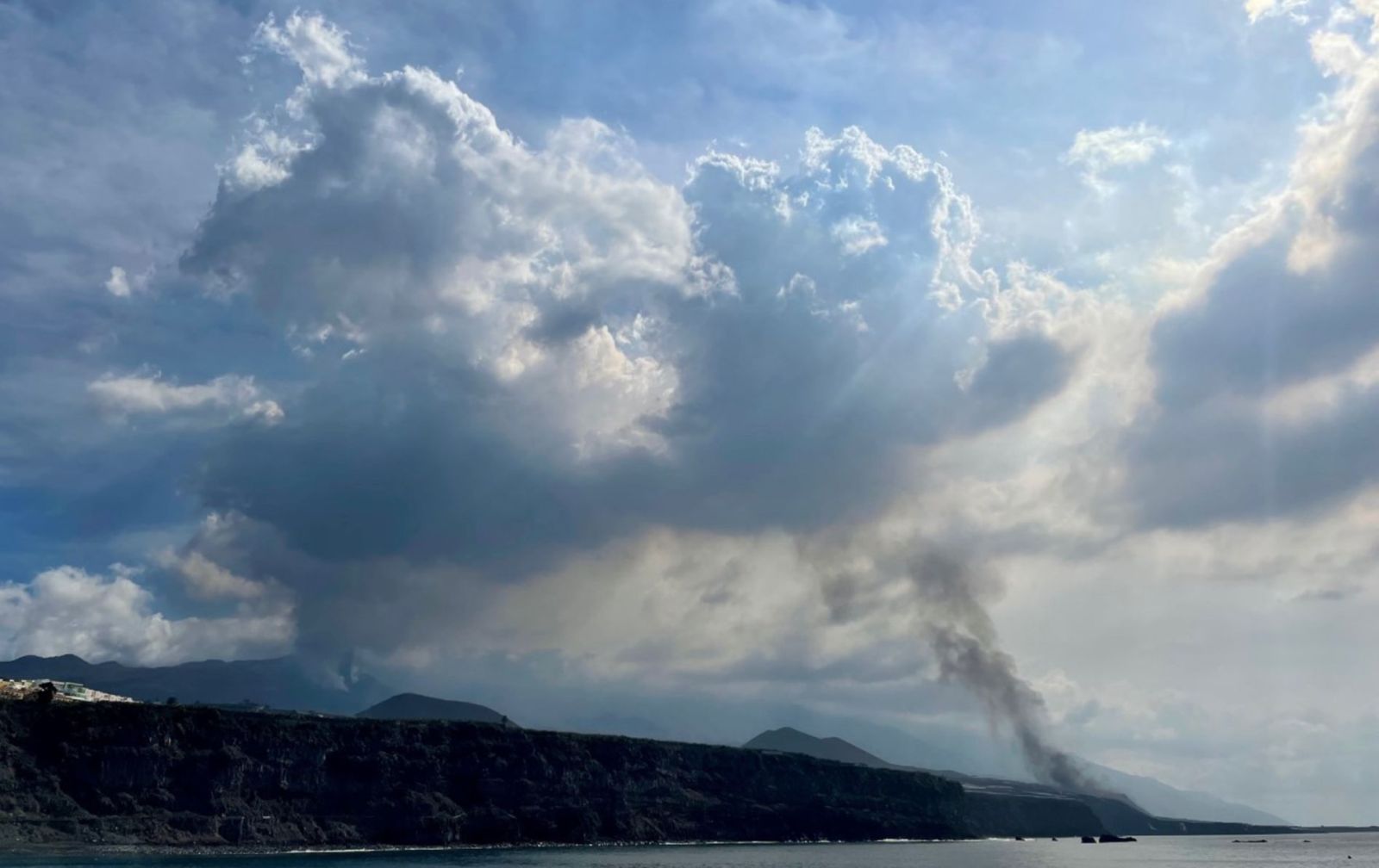 Vista del volcán de Cumbre Vieja  a la izquierda de la imagen,  con la fumarola negra de la lava que llega a la playa de Los Guirres desde el puerto de Tazacorte. | | LP/DLP