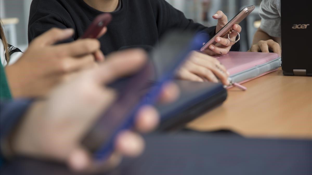 Unos estudiantes consultan sus teléfonos móviles en una clase.