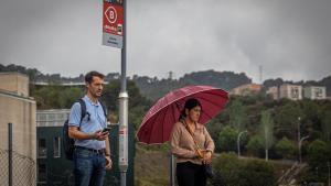 Dos usuarios del bus a demanda de Torre Baró esperan en una de las paradas del barrio