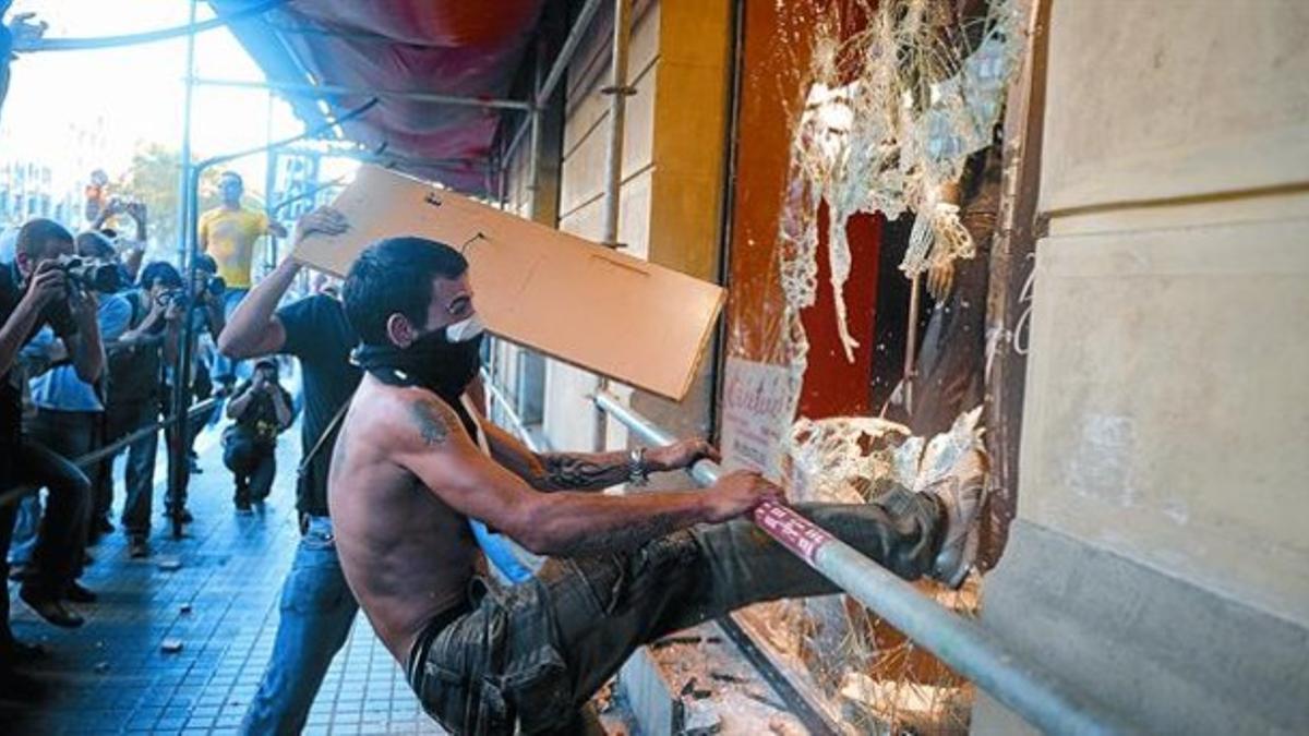 Dos jóvenes destrozan el escaparate de un local comercial en Barcelona, el 29-M.