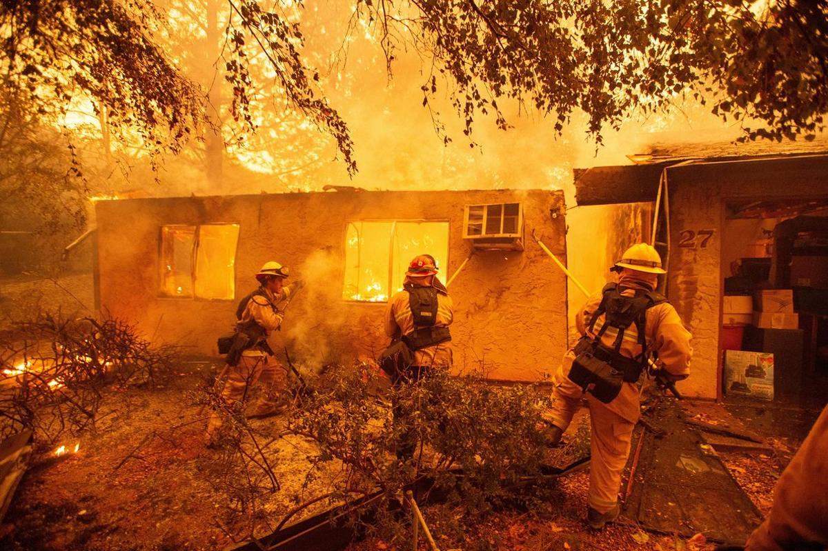 TOPSHOT - Firefighters push down a wall while battling against a burning apartment complex in Paradise, north of Sacramento, California on November 09, 2018. - A rapidly spreading, late-season wildfire in northern California has burned 20,000 acres of land and prompted authorities to issue evacuation orders for thousands of people. As many as 1000 homes, a hospital, a Safeway store and scores of other structures have burned in the area as the Camp fire tore through the region. (Photo by Josh Edelson / AFP)