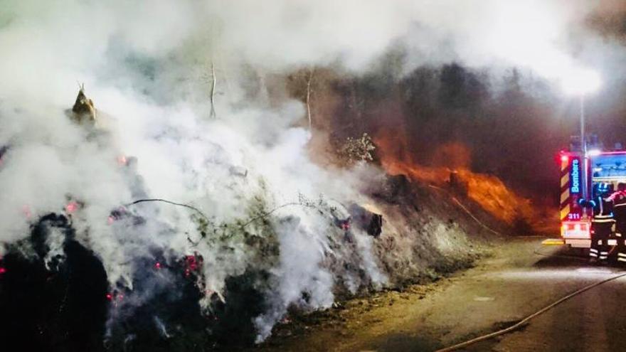 Los bomberos apagando el incendio en un margen de la carretera.