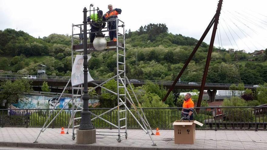 Tres operarios cambian una luminaria por otra de tecnología led en el puente que une Sama y La Felguera.