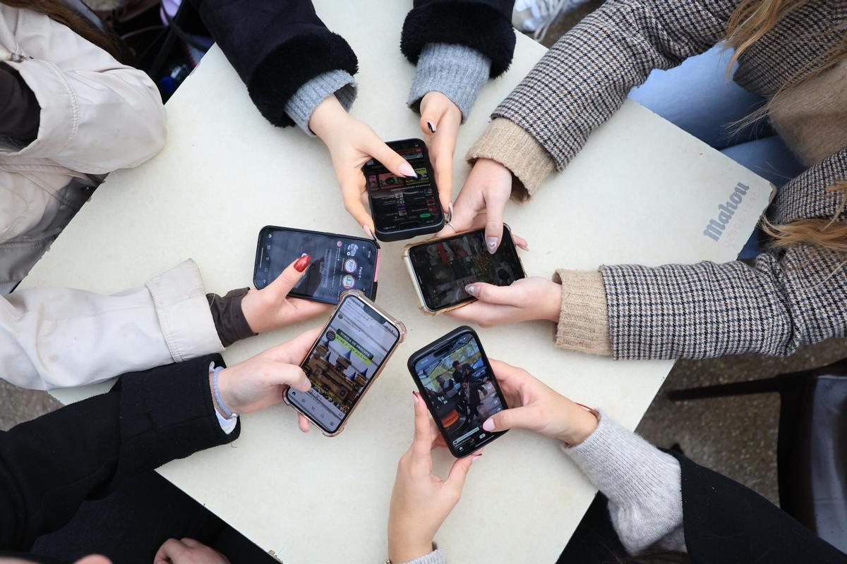 Varias jóvenes revisan sus redes sociales con sus teléfonos móviles.