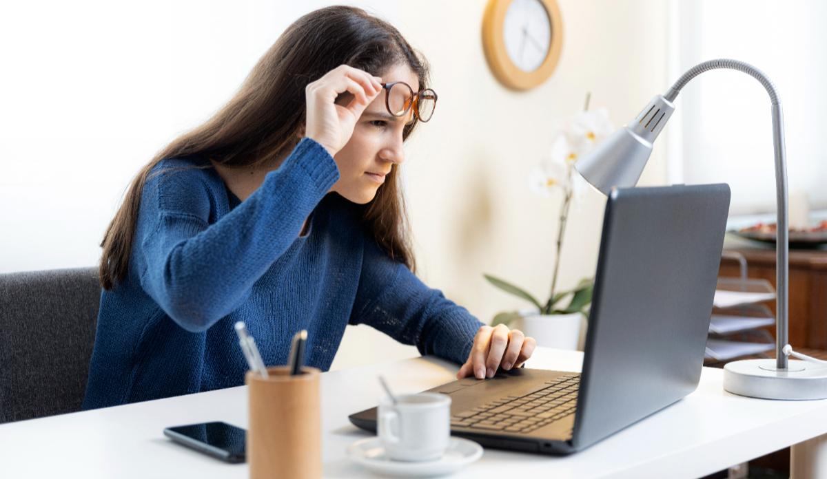 Una chica se retira las gafas con protección de luz azul delante de la pantalla de un ordenador.