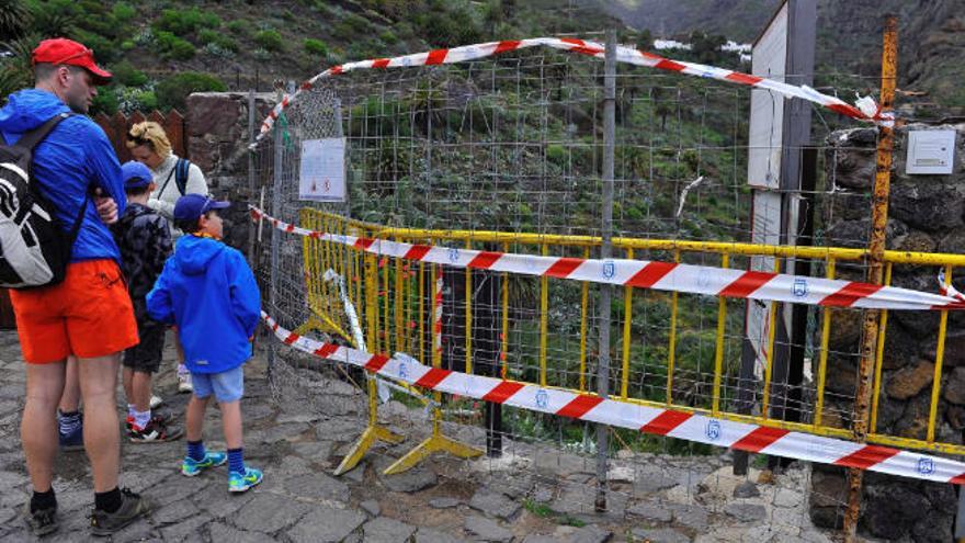 Una familia de turistas junto a la valla que impide el paso al sendero del barranco de Masca desde febrero de 2018.