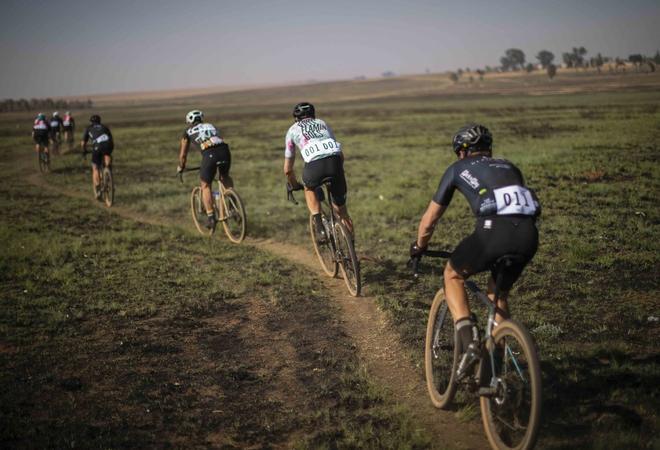 Un grupo de ciclistas líderes montan juntos en una sola pista durante la carrera inaugural de bicicletas de fondo de grava SouthxSoutheast en los caminos de tierra abiertos al sur de Johannesburgo, Sudáfrica.