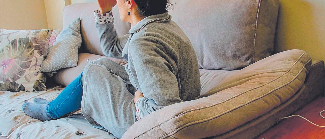 Una mujer realiza un gesto de dolor, recostada en un sofá.